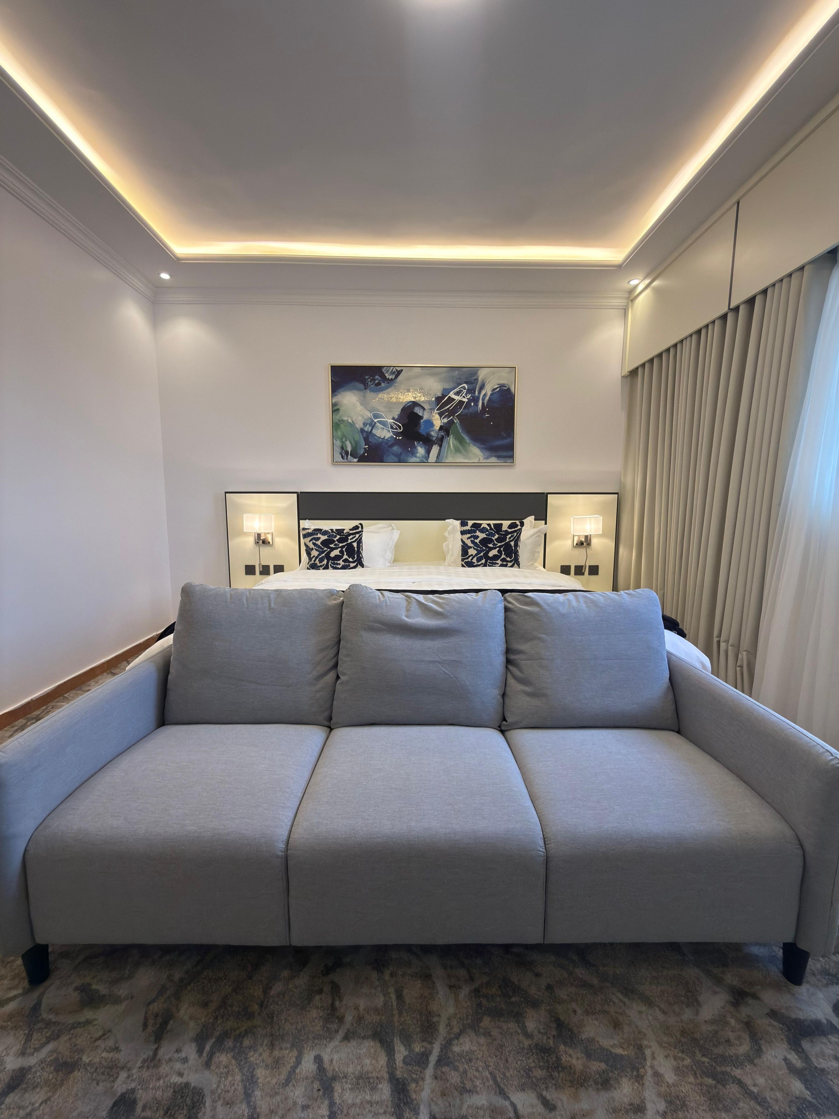A modern living room with a grey sofa, a painting above the sofa, and a patterned carpet.