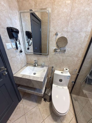 A bathroom with a marble sink, a toilet, a mirror, and a shower area. - Aurion Quba (Madinah)