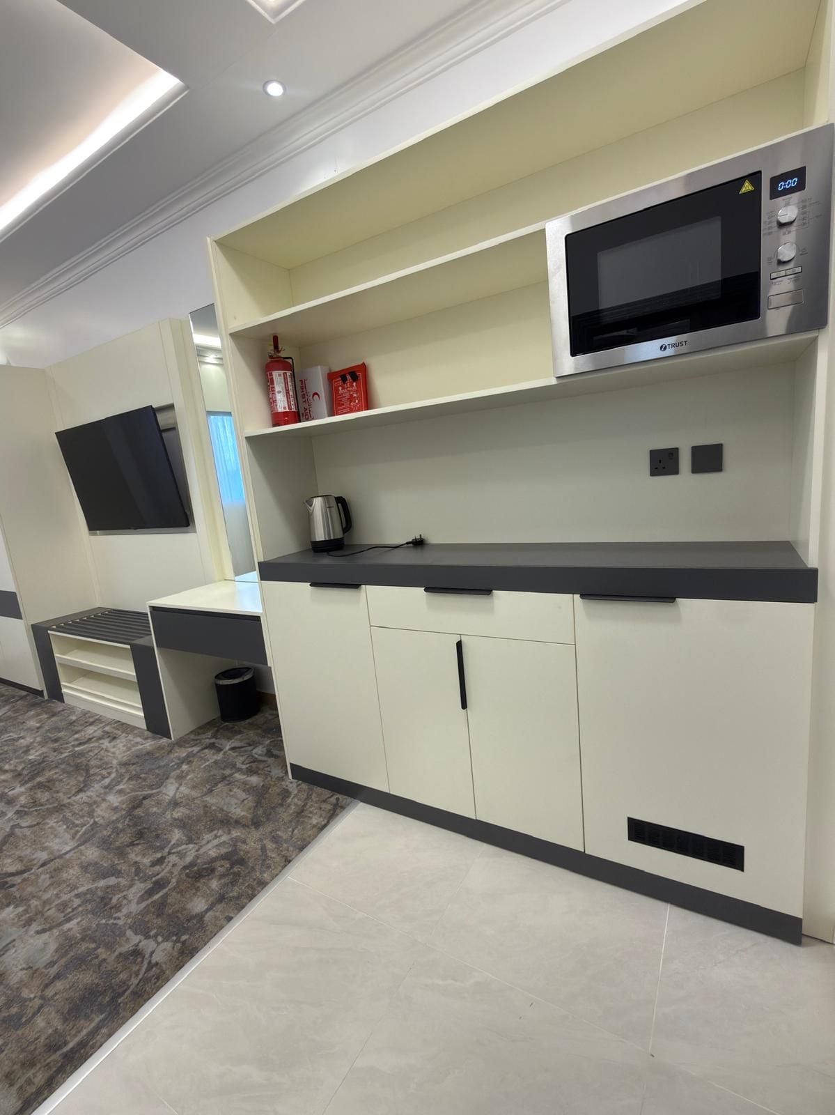 A modern kitchen with a built-in microwave, a kettle, and a shelf with fire extinguishers.