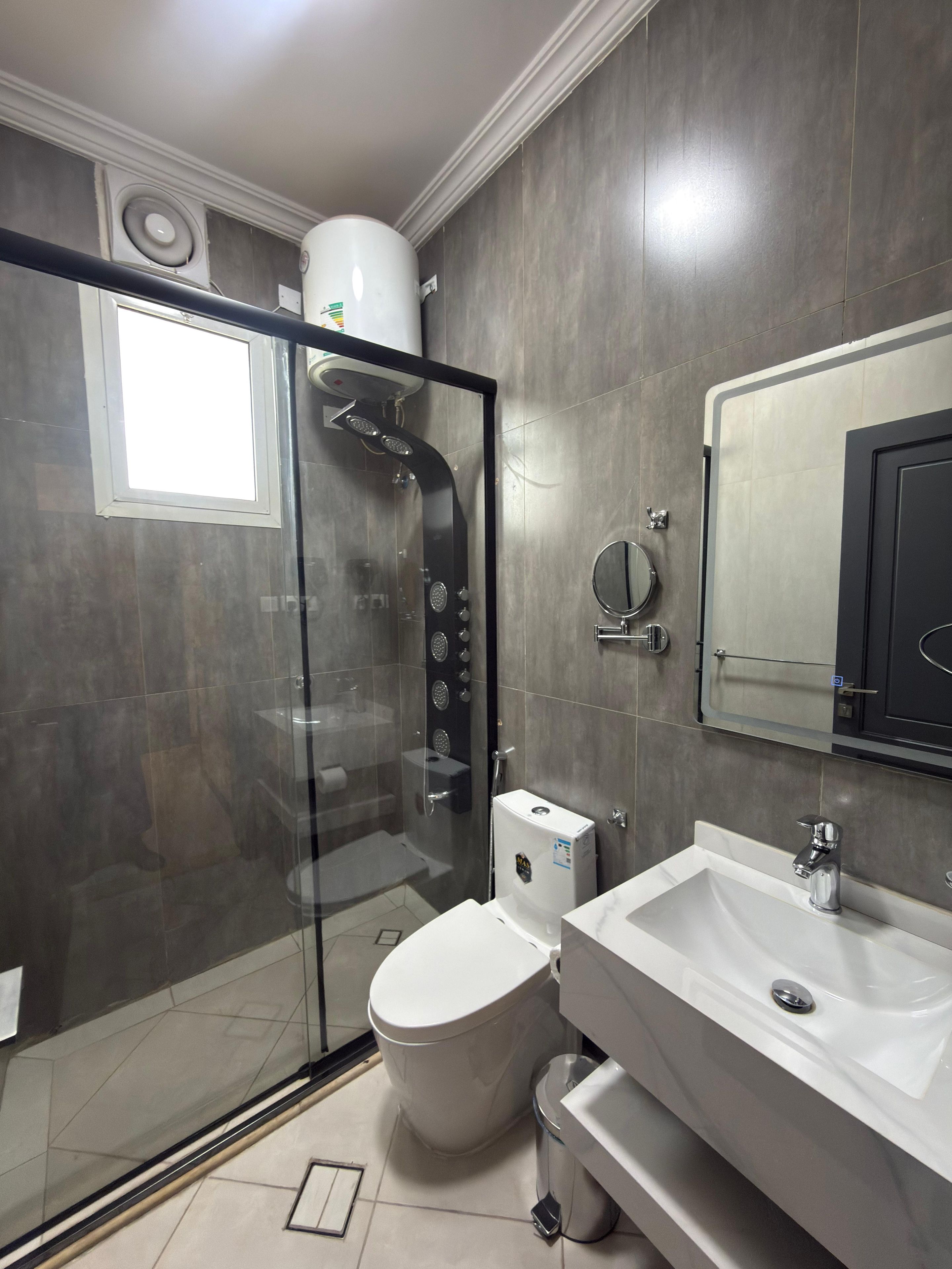 A modern bathroom with a glass-enclosed shower, a toilet, and a sink with a mirror above it.
