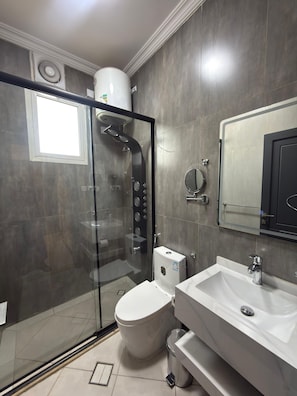 A modern bathroom with a glass-enclosed shower, a toilet, and a sink with a mirror above it. - Aurion Quba (Madinah)