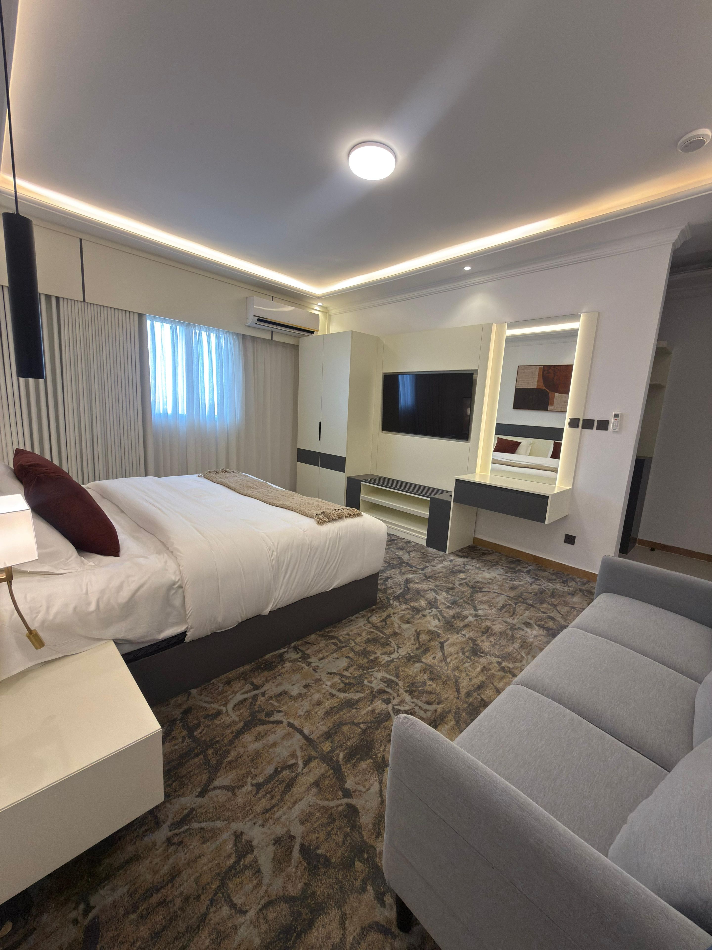 A hotel room with a bed, a desk, a chair, a TV, and a mirror.