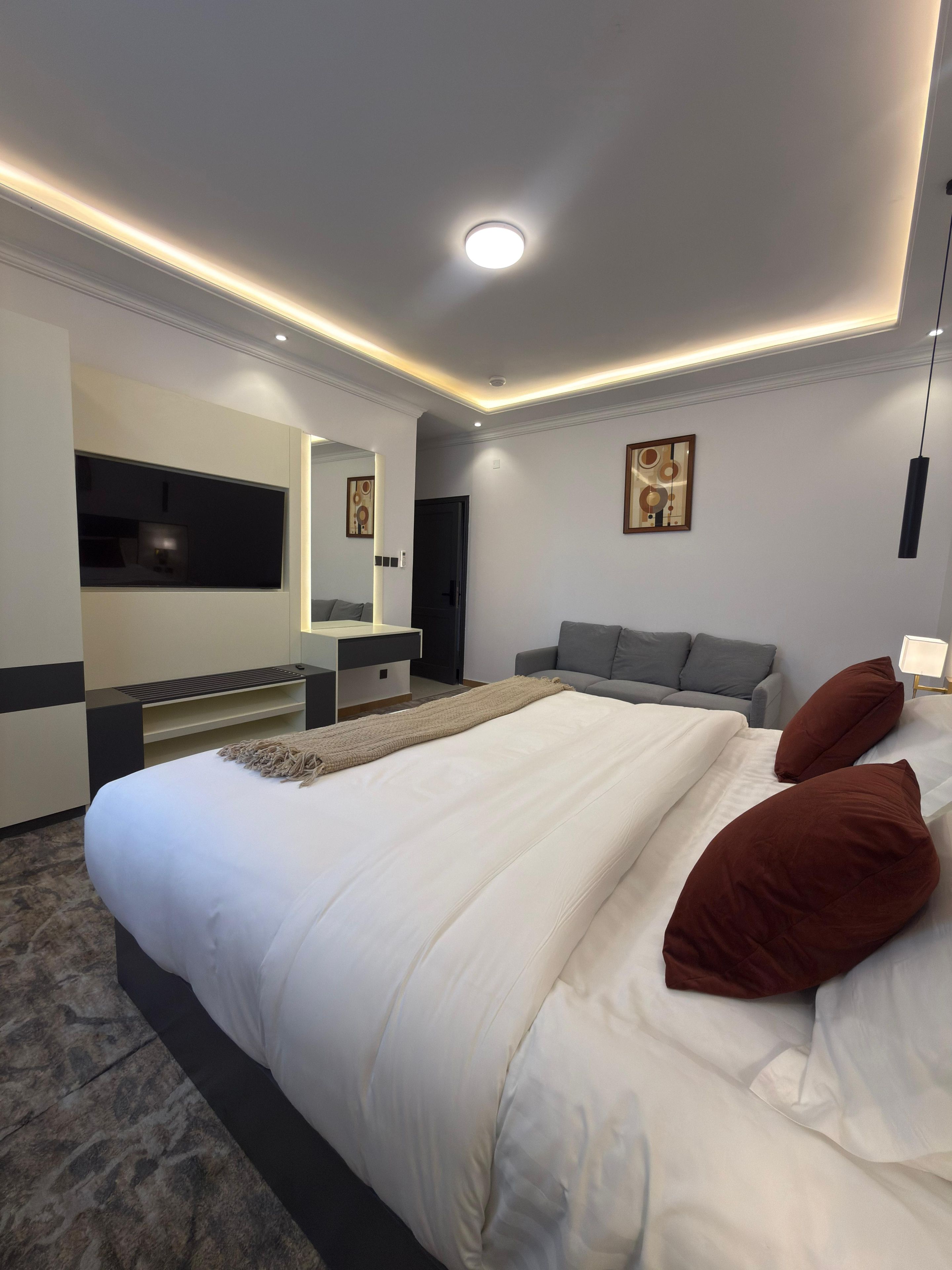 A modern hotel room with a large bed, a bedside table, a flat-screen TV, a sofa, and a painting on the wall.