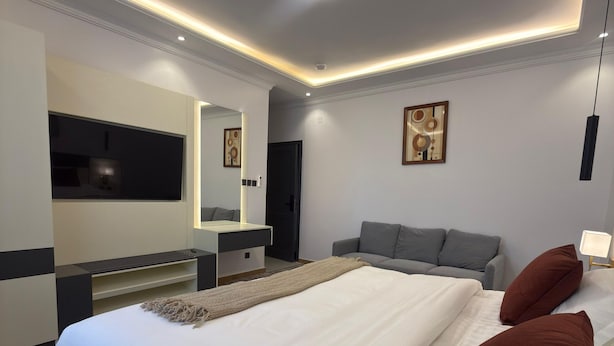 Ein modernes Hotelzimmer mit einem großen Bett, einem Nachttisch, einem Flachbildfernseher, einer Couch und einem Gemälde an der Wand.