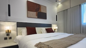 Ein modernes Hotelzimmer mit einem großen Bett, einem Kopfteil, Nachttischlampen, einem an der Wand hängenden abstrakten Gemälde und einem Fenster mit Vorhängen.