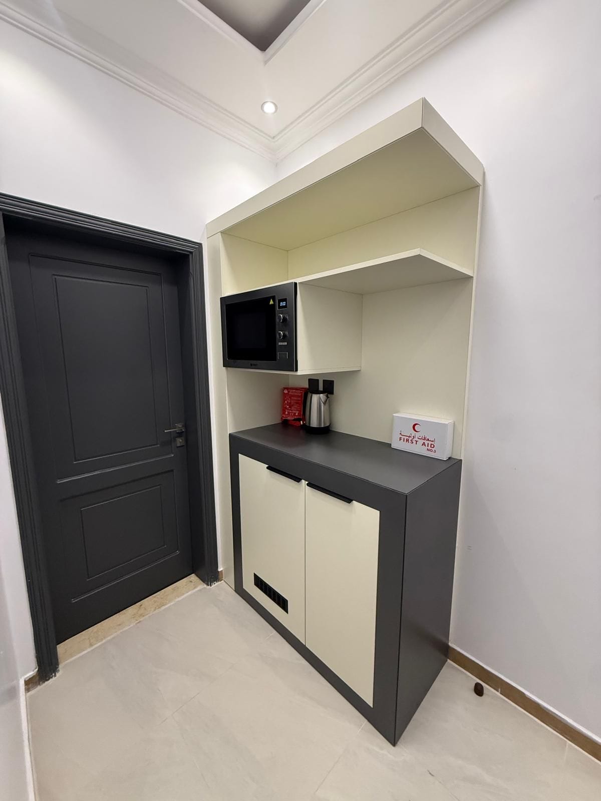 A compact kitchen with a microwave, a coffee maker, and a first aid kit on the counter.