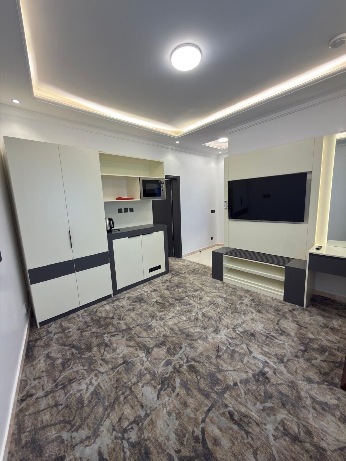 A modern kitchen with built-in appliances, a dining area with a flat-screen TV, and a patterned floor.