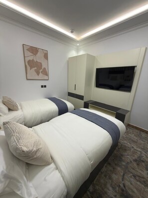 A hotel room with two beds, a TV, a wardrobe, and a ceiling light. - Aurion Quba (Madinah)