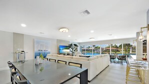 Un salon moderne avec une table à manger en verre, des canapés et une vue sur une piscine.
