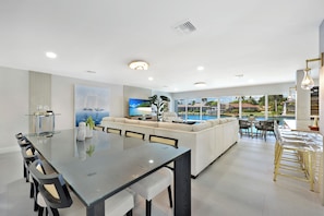 Una sala de estar moderna con una mesa de comedor de vidrio, sofás y vistas a una piscina.