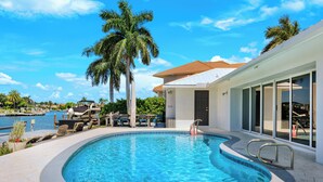 Une piscine à l’eau d’un bleu cristallin, entourée d’une terrasse aménagée avec des chaises longues et un palmier.