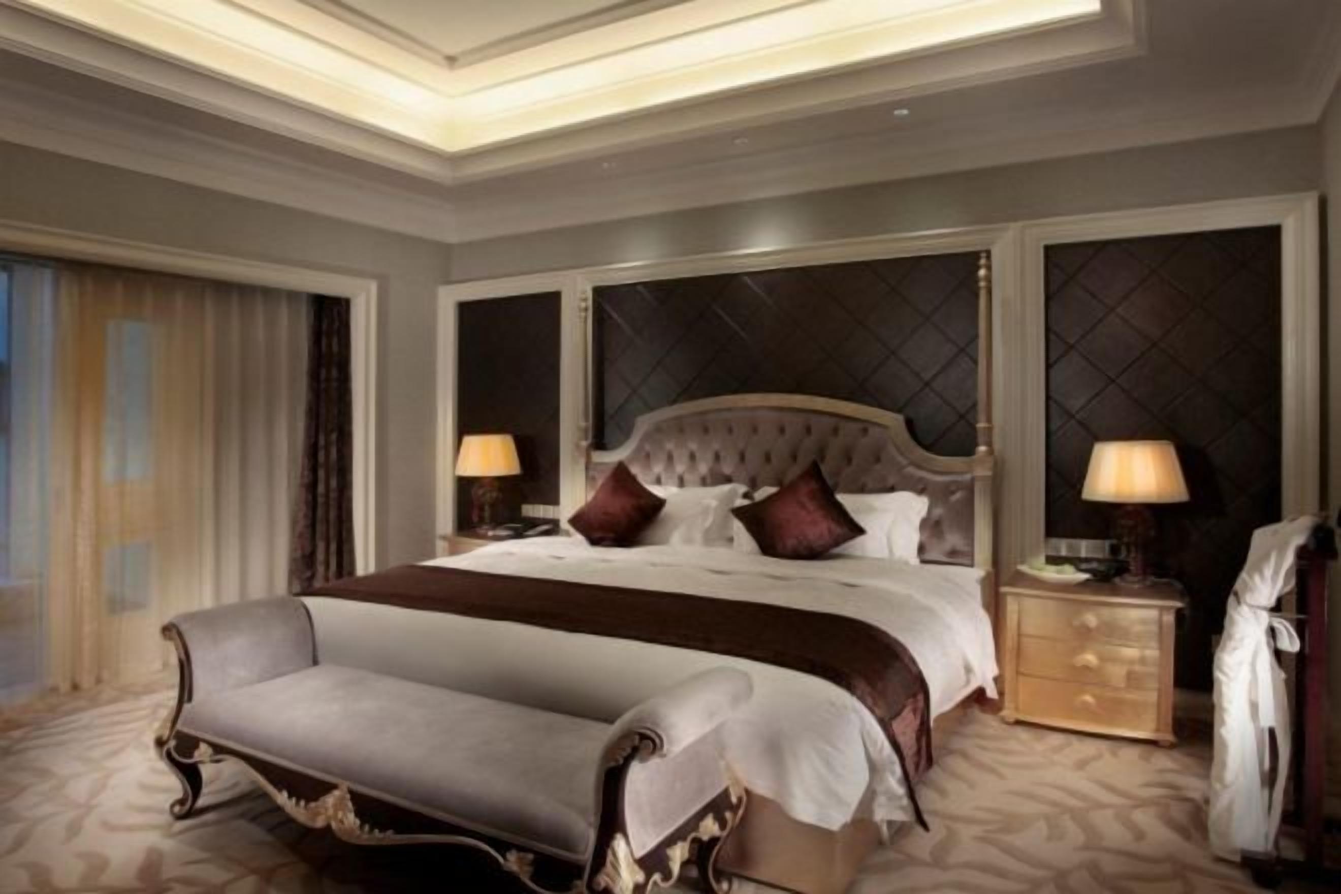 A spacious hotel room with a large bed, a sitting area, and a nightstand with lamps.