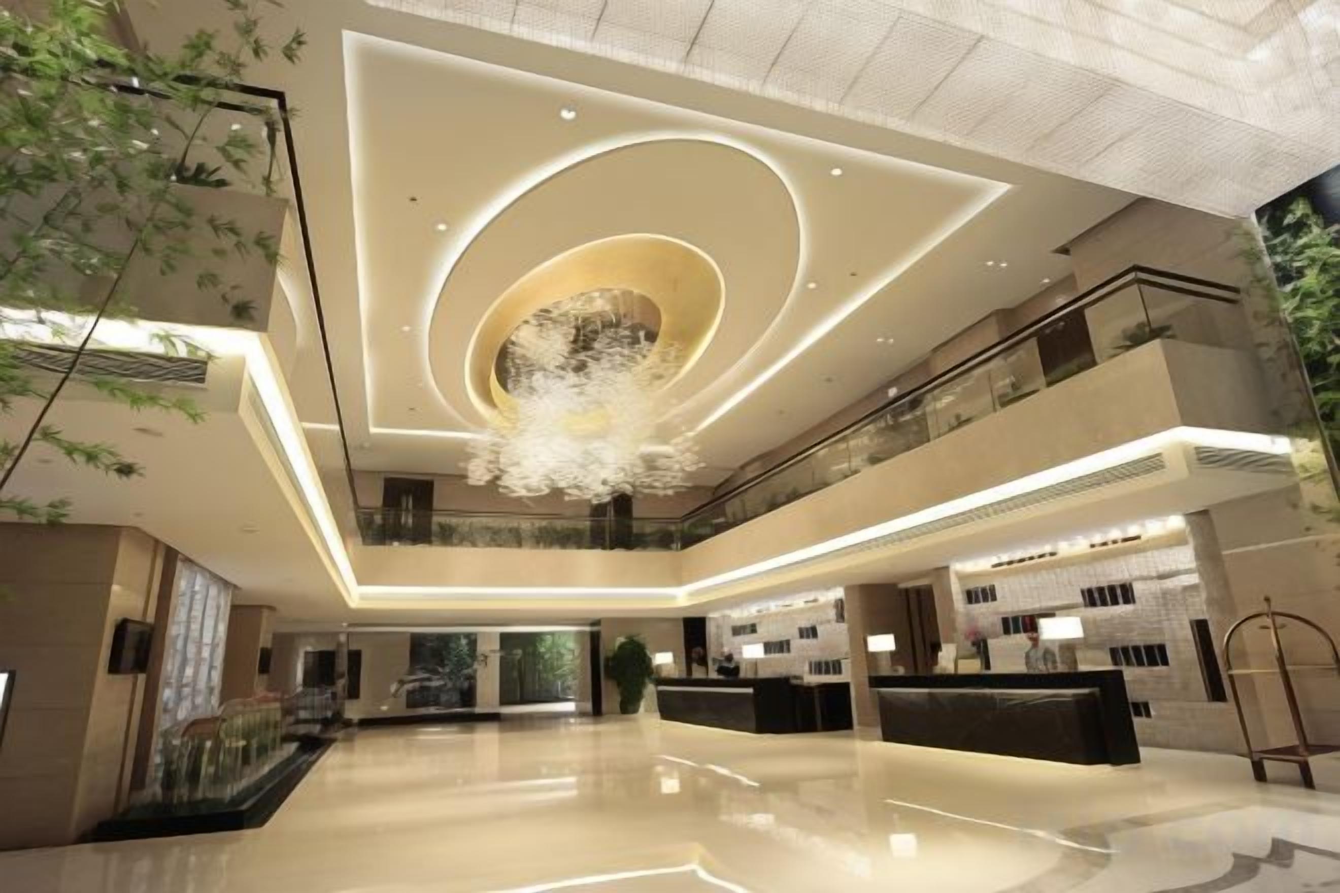 Un hall d’hôtel moderne avec un comptoir d’accueil central, plusieurs étages et un luminaire décoratif au plafond.