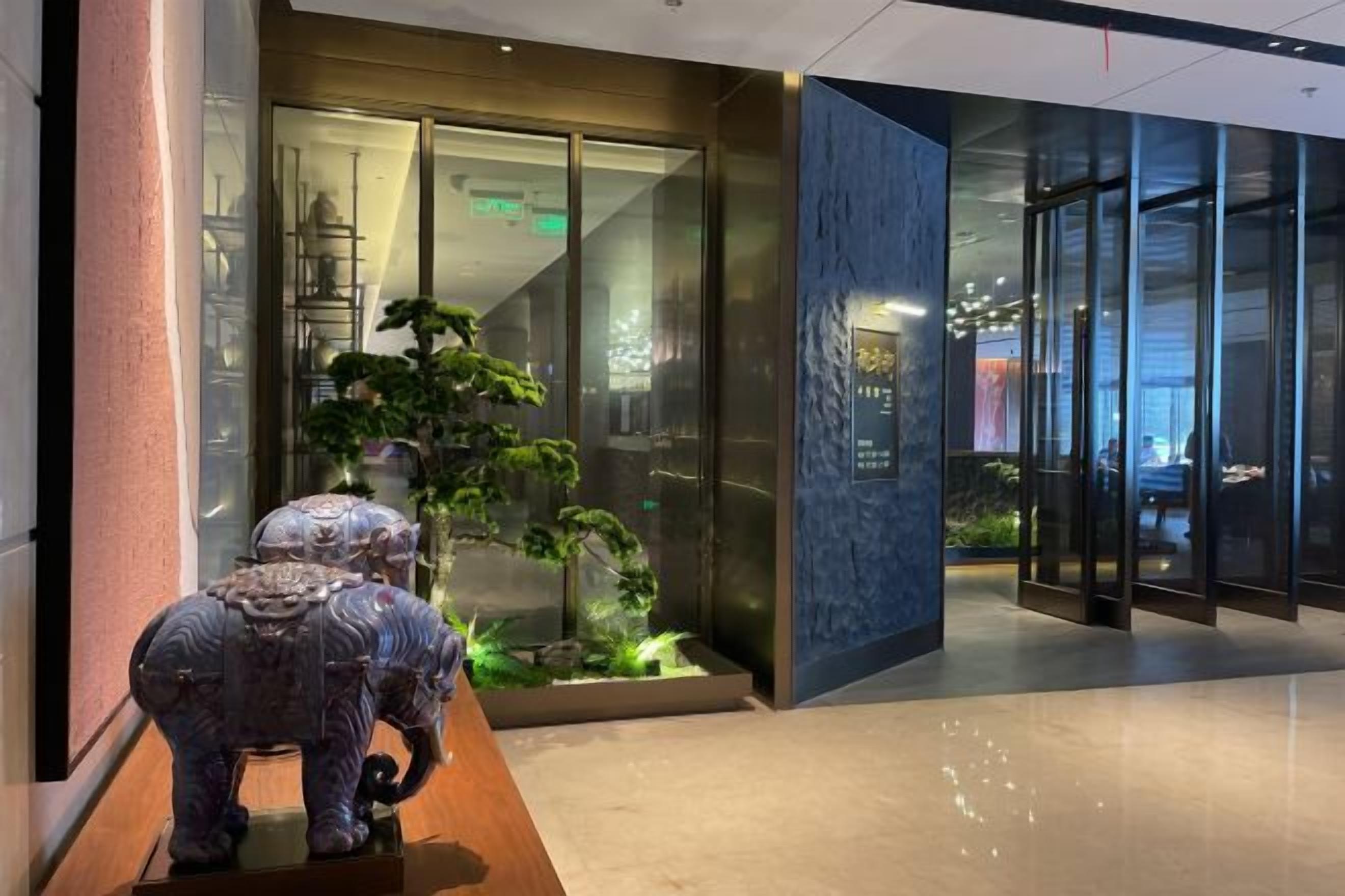 A reception area with a glass door entrance, a small indoor garden, and a statue of an elephant.