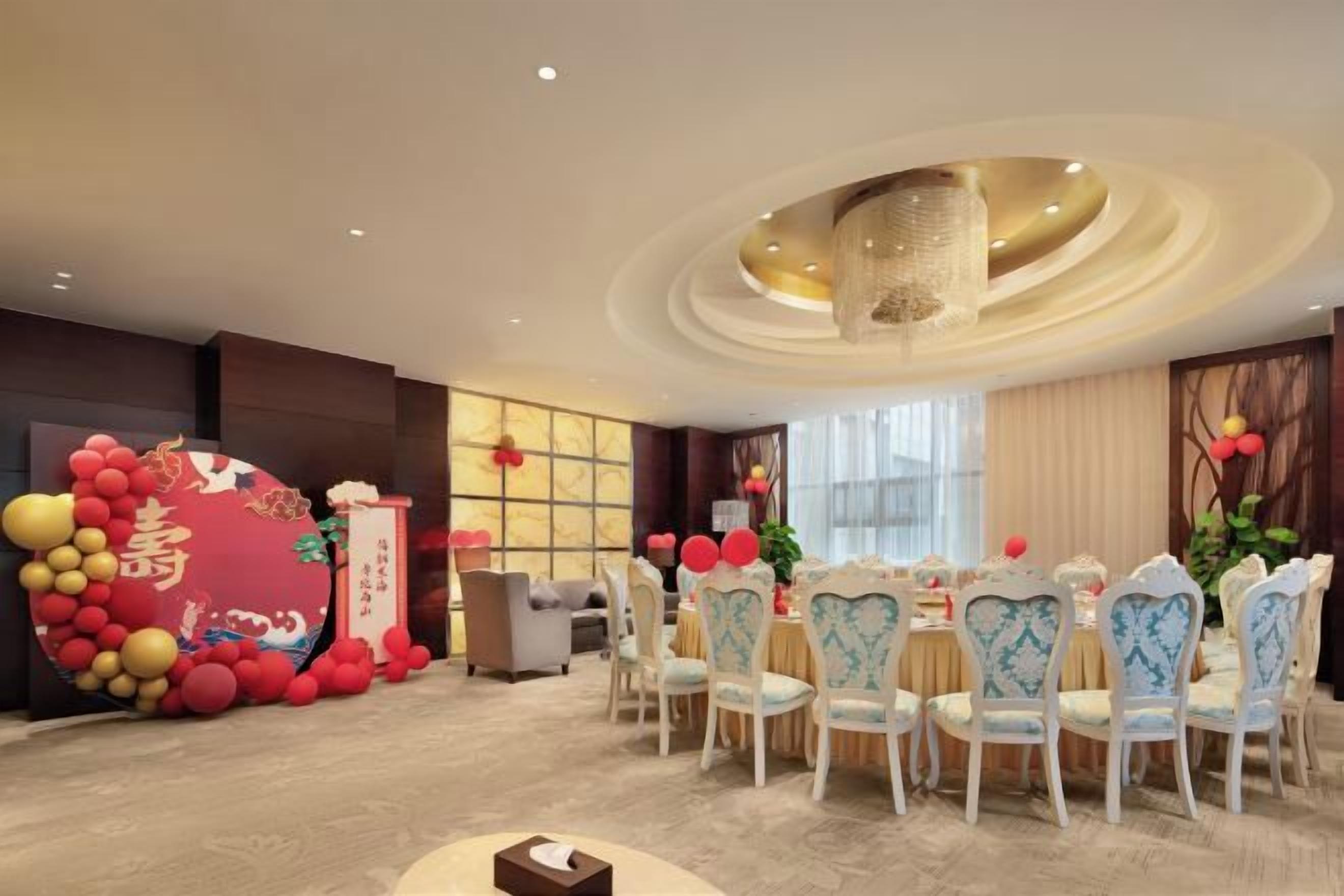 A dining area with round tables, chairs, and a decorative balloon arch.