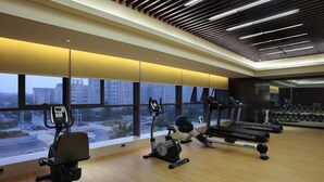 Ein Fitnessstudio mit Laufbändern, Krafttrainingsgeräten und großen Fenstern mit Blick auf die Stadt.
