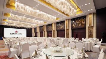 Une salle de banquet avec des tables rondes, des chaises blanches et un grand écran à l’avant.