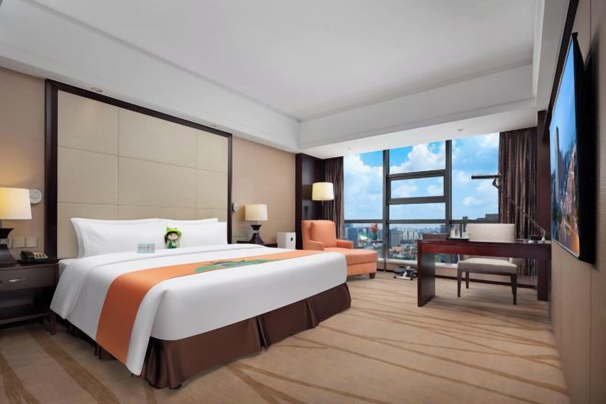 A hotel room with a large bed, a desk, a chair, and a view of the city.