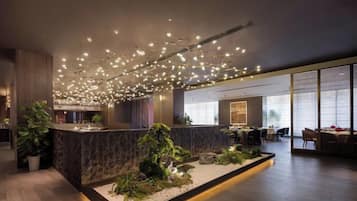 A modern hotel lobby with a reception desk, seating area, and a large window.