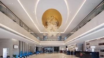 A spacious lobby with a high ceiling, a central chandelier, and a reception desk.