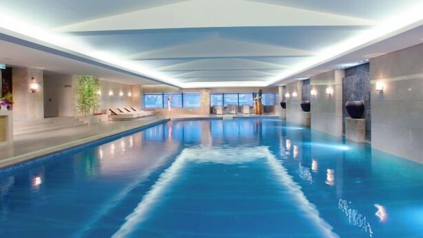Ein Innenpool mit länglicher Form, umgeben von Wänden mit Fenstern und einer Decke mit Einbaustrahlern.