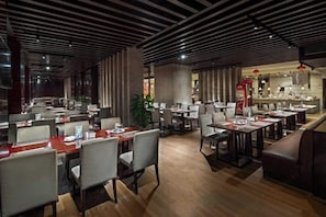 A modern restaurant interior with multiple dining tables and chairs, a kitchen area, and a seating area with a sofa.