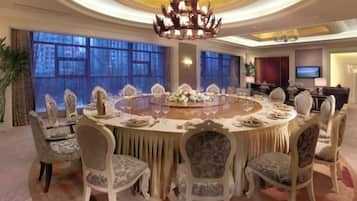 A round dining table with chairs, a chandelier, and large windows.