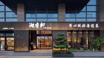A modern building facade with a large entrance, signage, and a well-maintained outdoor area with plants.
