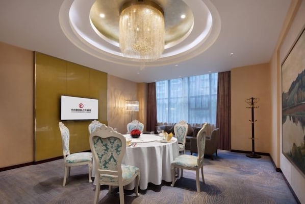 A conference room with a round table, chairs, a chandelier, and a large window.