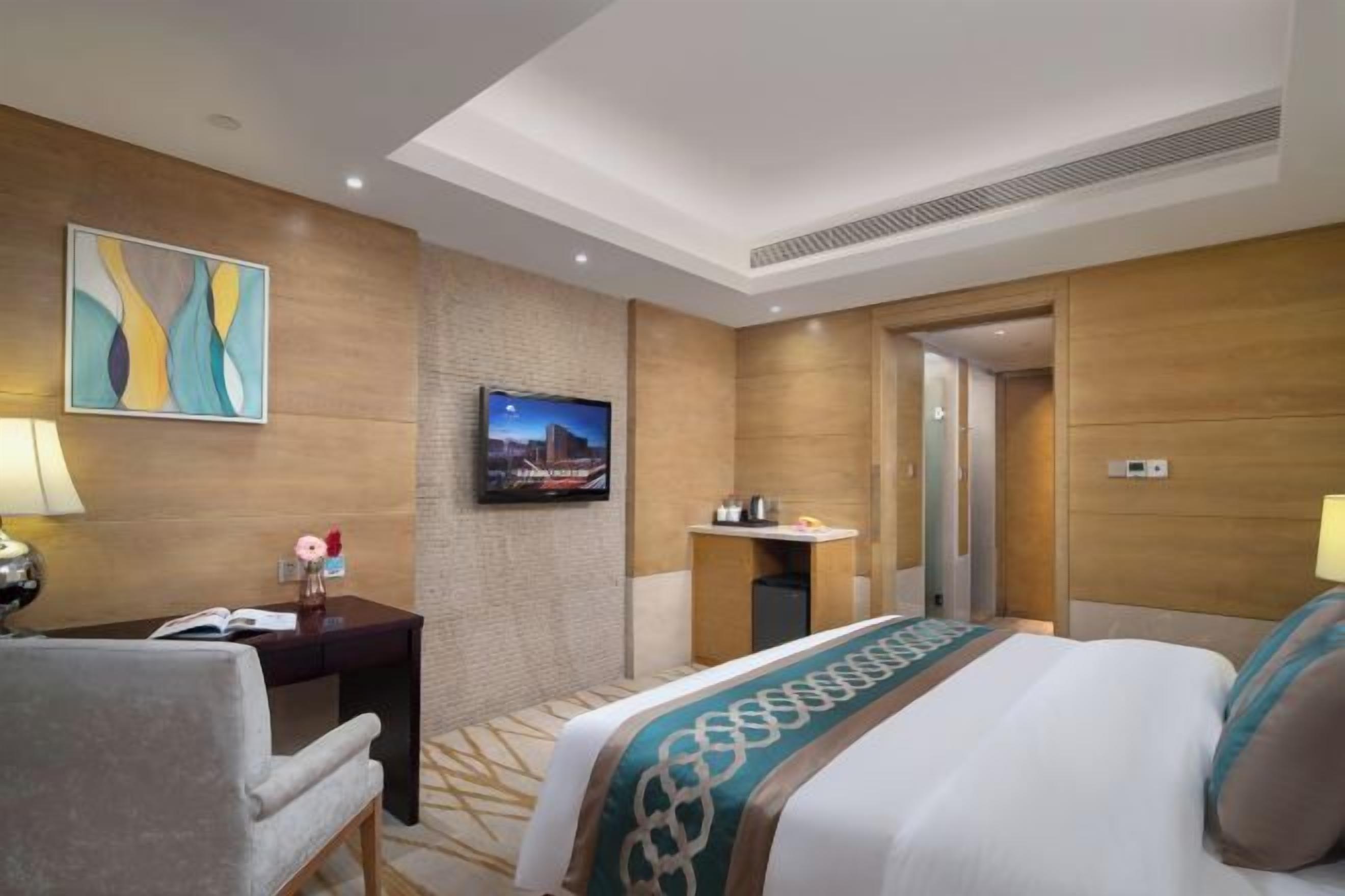 A hotel room with a bed, a desk, a chair, a TV, and a bathroom door.