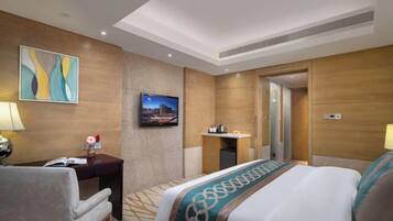 A hotel room with a bed, a desk, a chair, a TV, and a bathroom door.