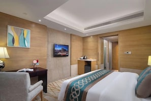 A hotel room with a bed, a desk, a chair, a TV, and a bathroom door.