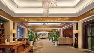 A hotel lobby with a chandelier, wooden furniture, potted plants, and a carpeted floor.