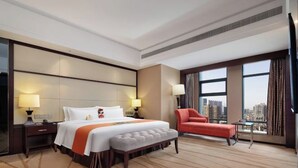 Ein Hotelzimmer mit einem großen Bett, einem roten Sessel, einem kleinen Tisch und Blick auf die Stadt.