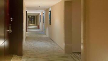 Un couloir d’hôtel avec un tapis à motifs, des portes des deux côtés et des tableaux encadrés accrochés aux murs.