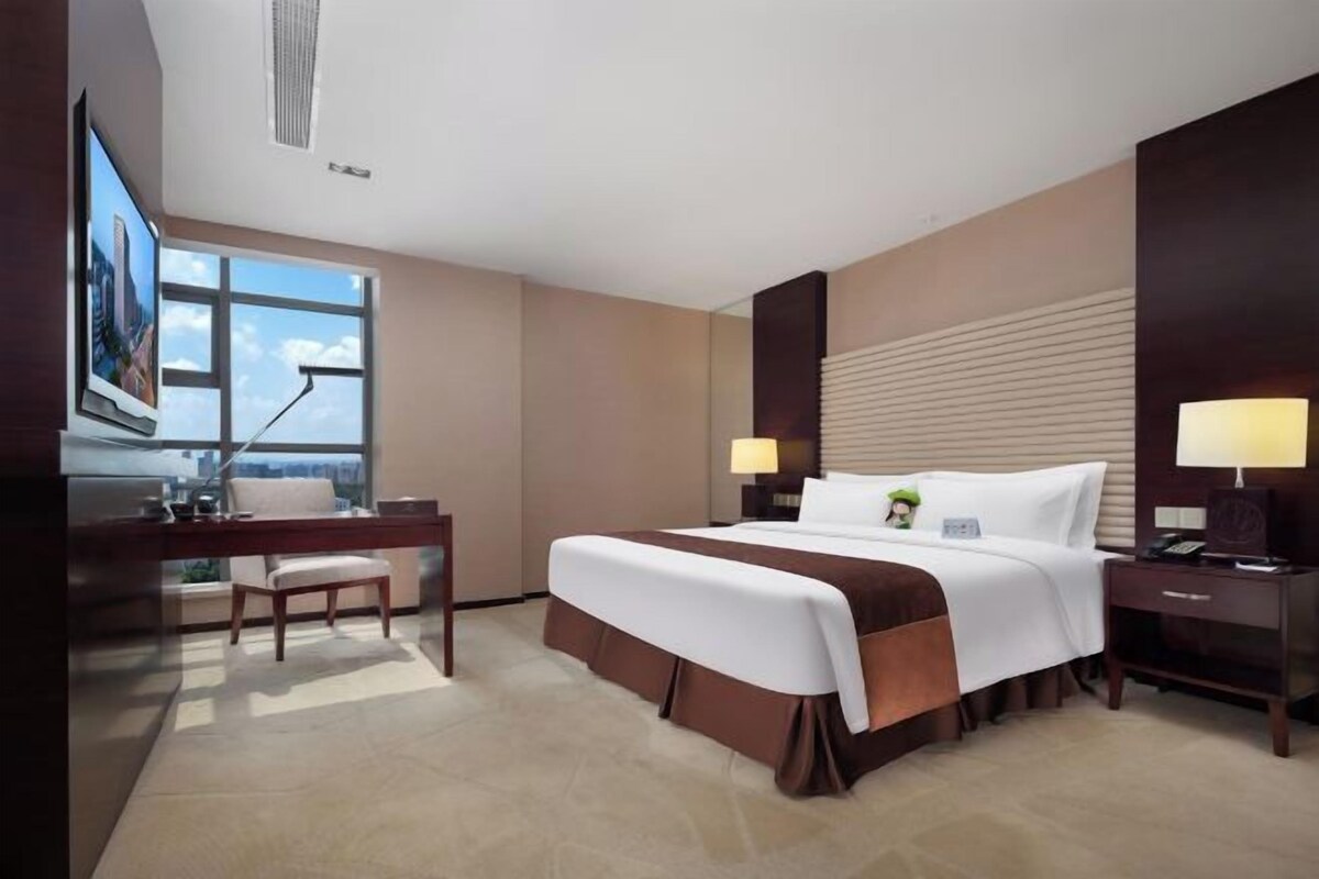 A hotel room with a large bed, a desk, a chair, and a TV.