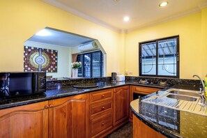 A kitchen with wooden cabinets, a black countertop, a microwave, and a window with a view. - Classic 5BR Villa with Pool&Gardens(SP1) (Pattaya City,South Pattaya)