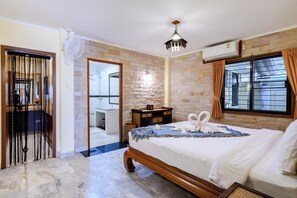 A hotel room with a bed, a wooden nightstand, a mirror, a window with curtains, and a bathroom visible through an open door. - Classic 5BR Villa with Pool&Gardens(SP1) (Pattaya City,South Pattaya)