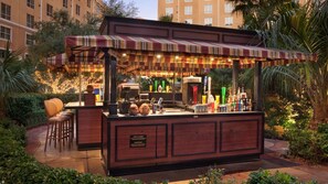 Eine Tiki-Bar im Freien mit einem Streifenmarkisen, einer Theke und Hockstühlen.