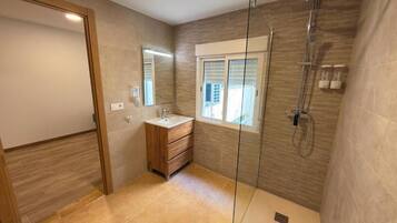 Un baño moderno con cabina de ducha de vidrio, tocador de madera y ventana que deja entrar luz natural.