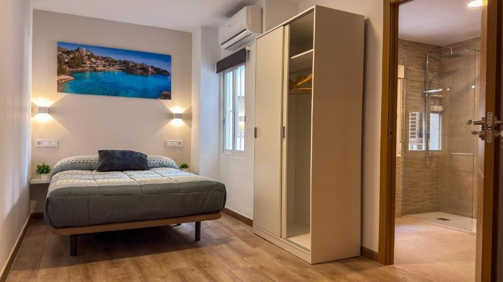 Un dormitorio con cama, mesita de noche, lámpara, armario y cabina de ducha de vidrio.