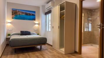 Un dormitorio con cama, mesita de noche, lámpara, armario y cabina de ducha de vidrio.
