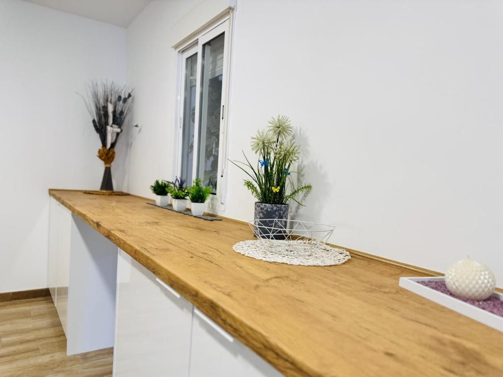 Une cuisine dotée d’un plan de travail en bois, de meubles blancs, d’une fenêtre et de diverses plantes en pot.