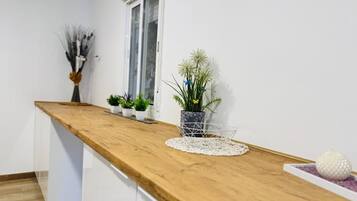 Une cuisine dotée d’un plan de travail en bois, de meubles blancs, d’une fenêtre et de diverses plantes en pot.