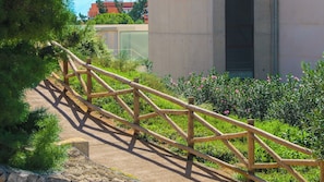 A wooden pedestrian bridge with a concrete pathway, surrounded by greenery and a modern building in the background.