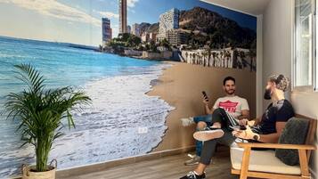Una habitación con un mural de playa, una planta en maceta y una silla de madera.