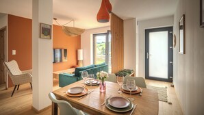 A dining area with a wooden table set for four, a sofa, and a view of a garden through a large window. - Vrbo Property (Bernardvillé)