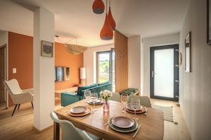 Un coin repas avec une table en bois dressée pour quatre personnes, un canapé et une vue sur un jardin par le biais d’une grande fenêtre.