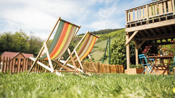 Two striped lounge chairs in a grassy area with a wooden deck and a table with a bottle and glasses. - Vrbo Property (Bernardvillé)