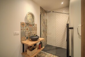 Ein Badezimmer mit einem großen Waschbecken, einem Spiegel, einer Dusche mit Glastür und gemusterten Fliesen an den Wänden.
